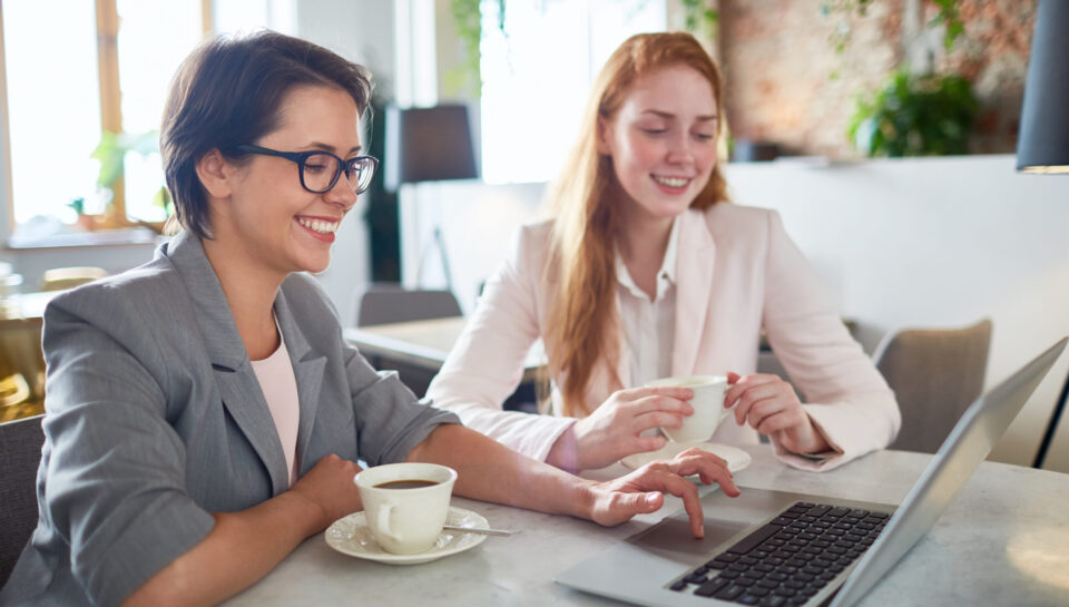 Two restful businesswomen looking through online shops assortment while having coffee in cafe